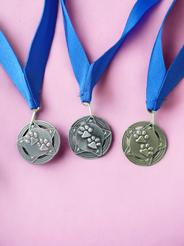 Bronze, Silver and Gold Medals on a pink background. The medals have two paw prints on a star background. The background of the photo is pink.
